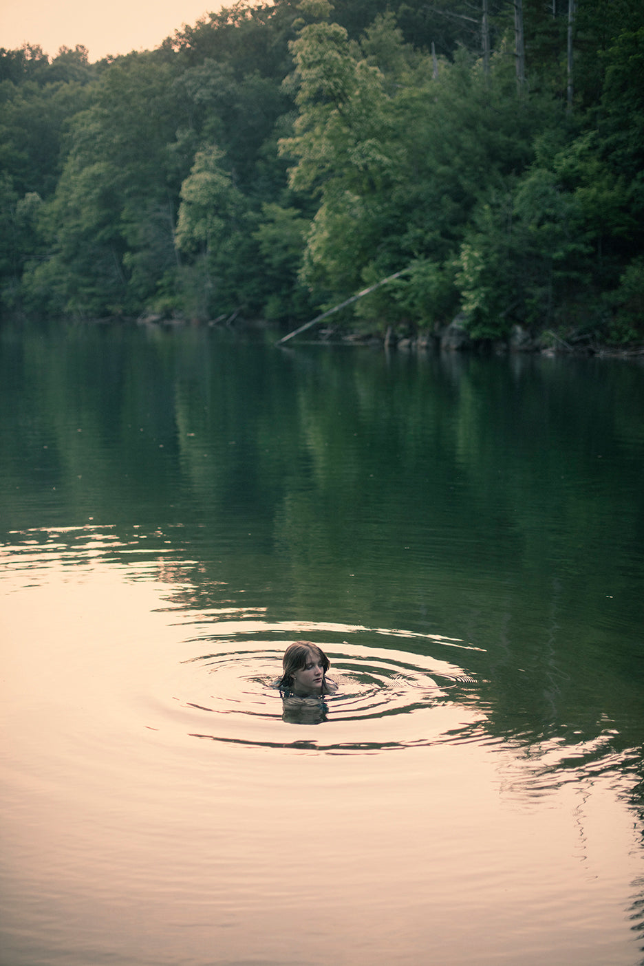 A photograph capturing a serene nature scene with a person in the water, surrounded by trees and a reflective lake.