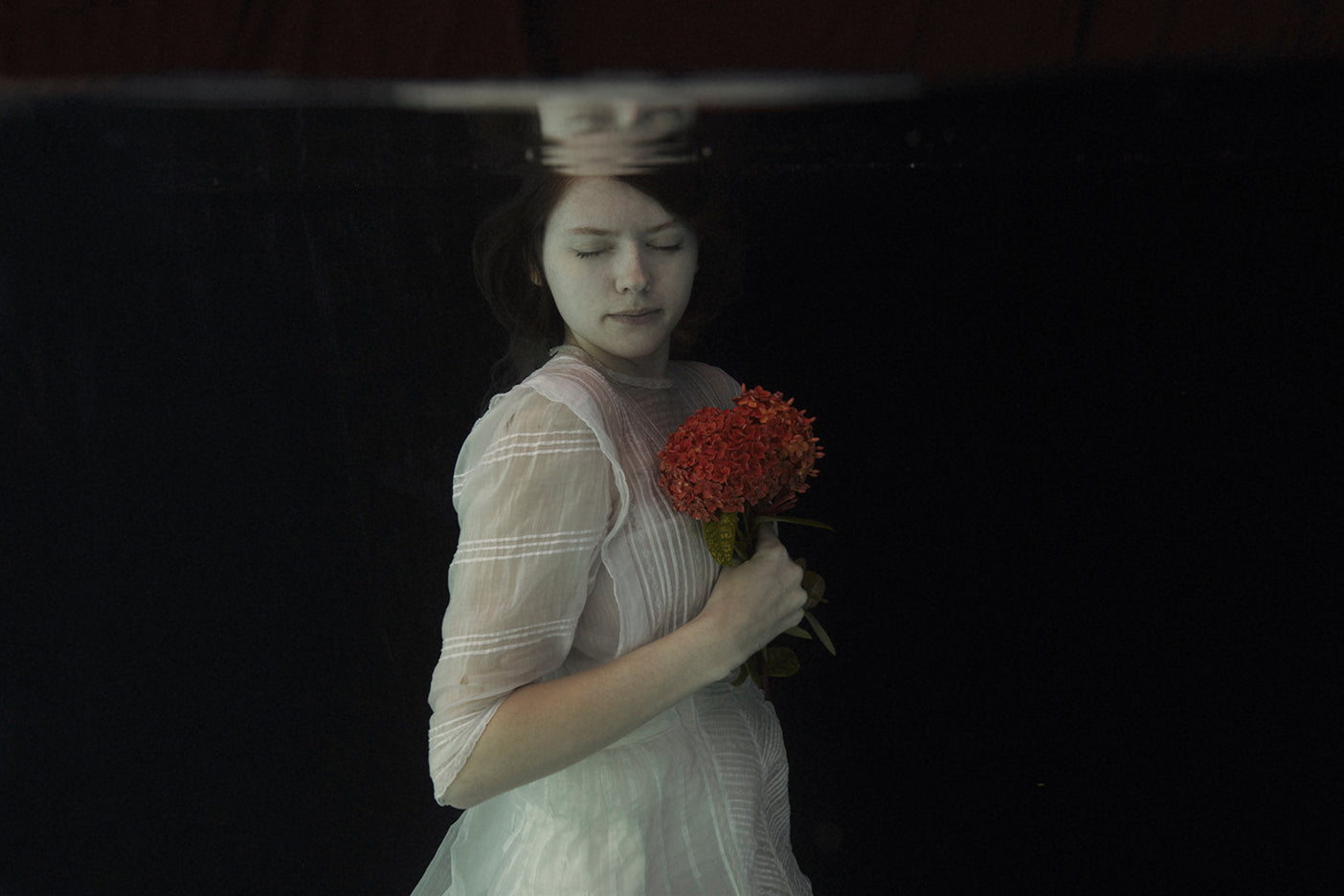 Underwater photograph of a person holding a red flower, with a serene and ethereal ambiance
