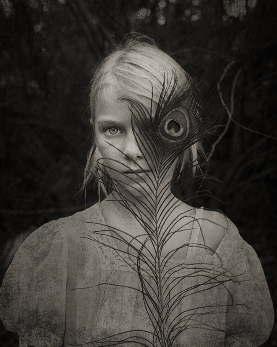 black and white photo of girl with peacock feather in front of one eye
