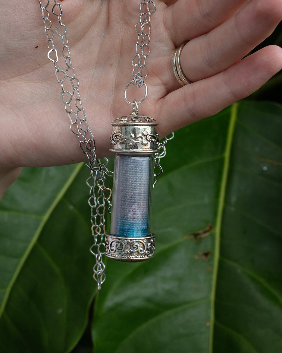 A silver metal adjustable heart-shaped chain necklace with a glass capsule pendant featuring a photograph and the word azure