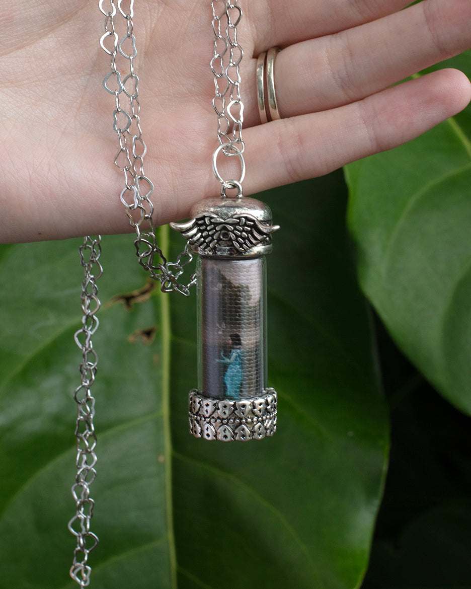 A silver metal adjustable heart-shaped chain necklace with a glass capsule pendant featuring a photograph and the word 'Beloved'.