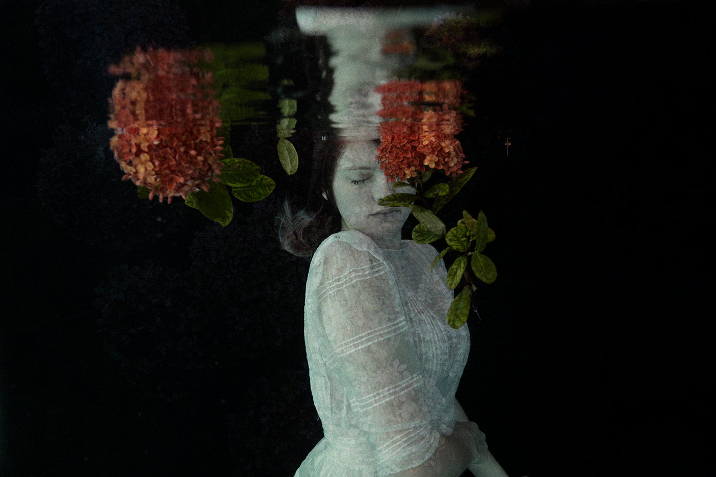 An ethereal photograph featuring a figure underwater with red floral elements, capturing a whimsical and mystical theme.