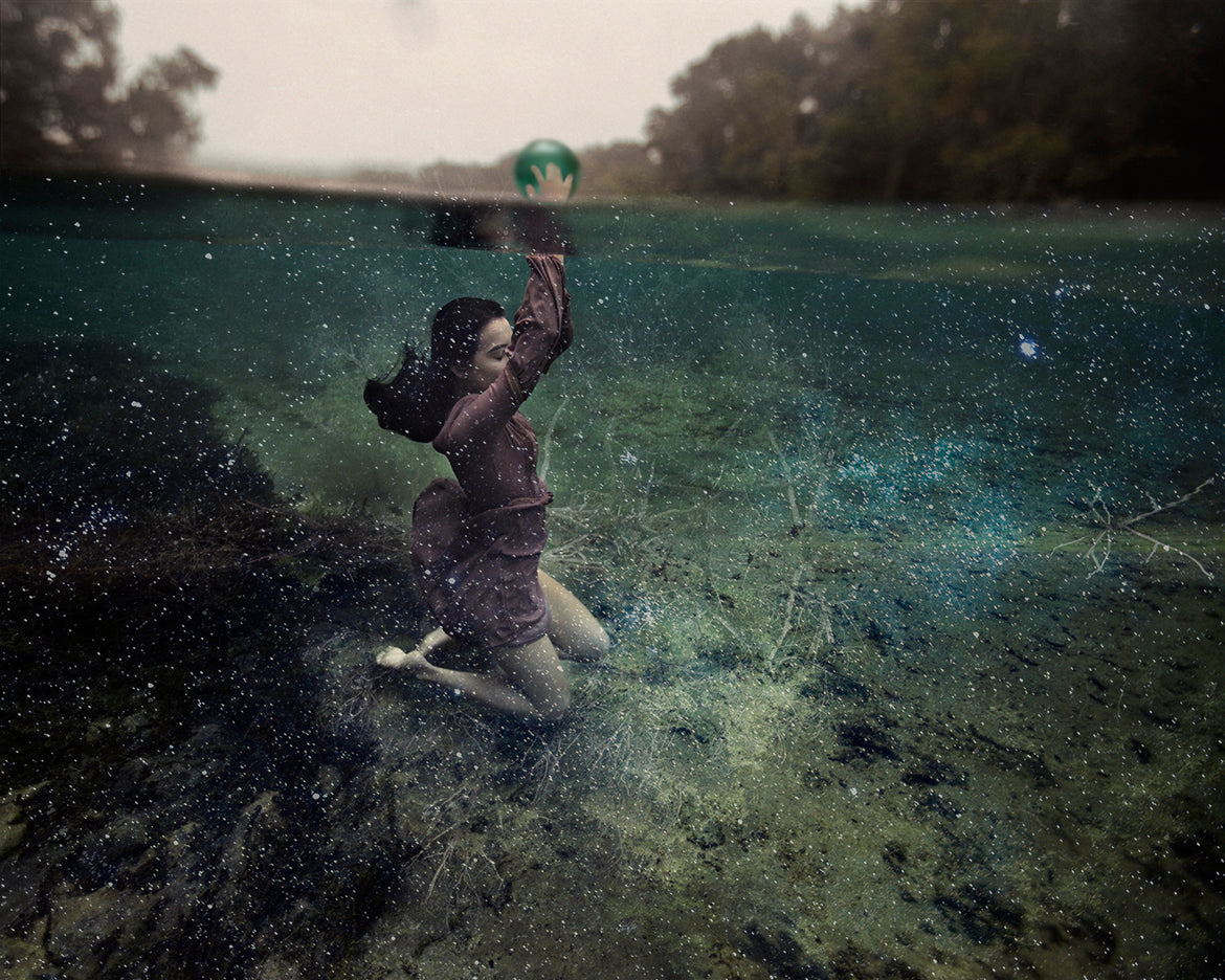 A photograph featuring a girl underwater, holding a glass orb, with a background of scattered stars creating a celestial ambiance.