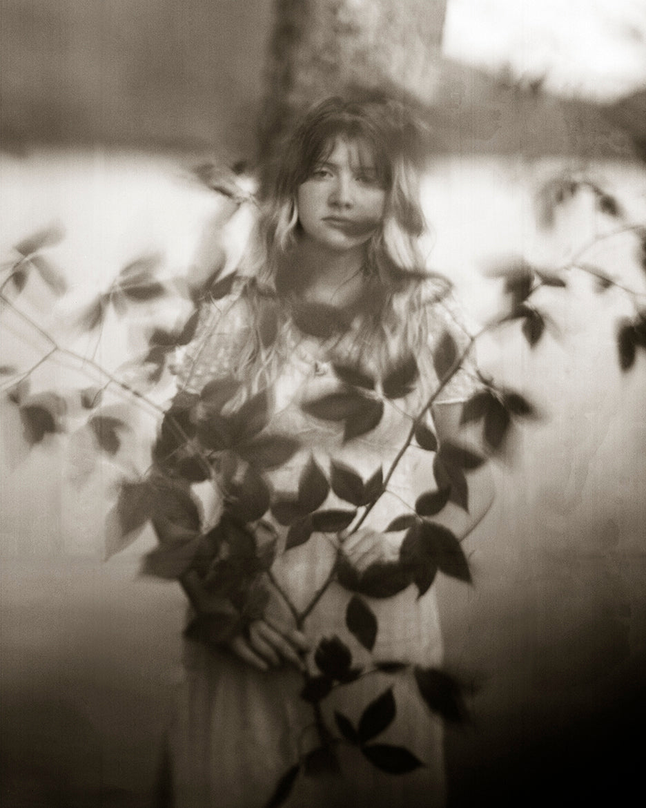 A black and white photograph of a girl with leaves, evoking a sense of nature and spirituality.