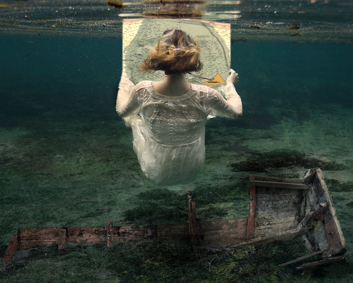 girl underwater with wrecked boat holding a map