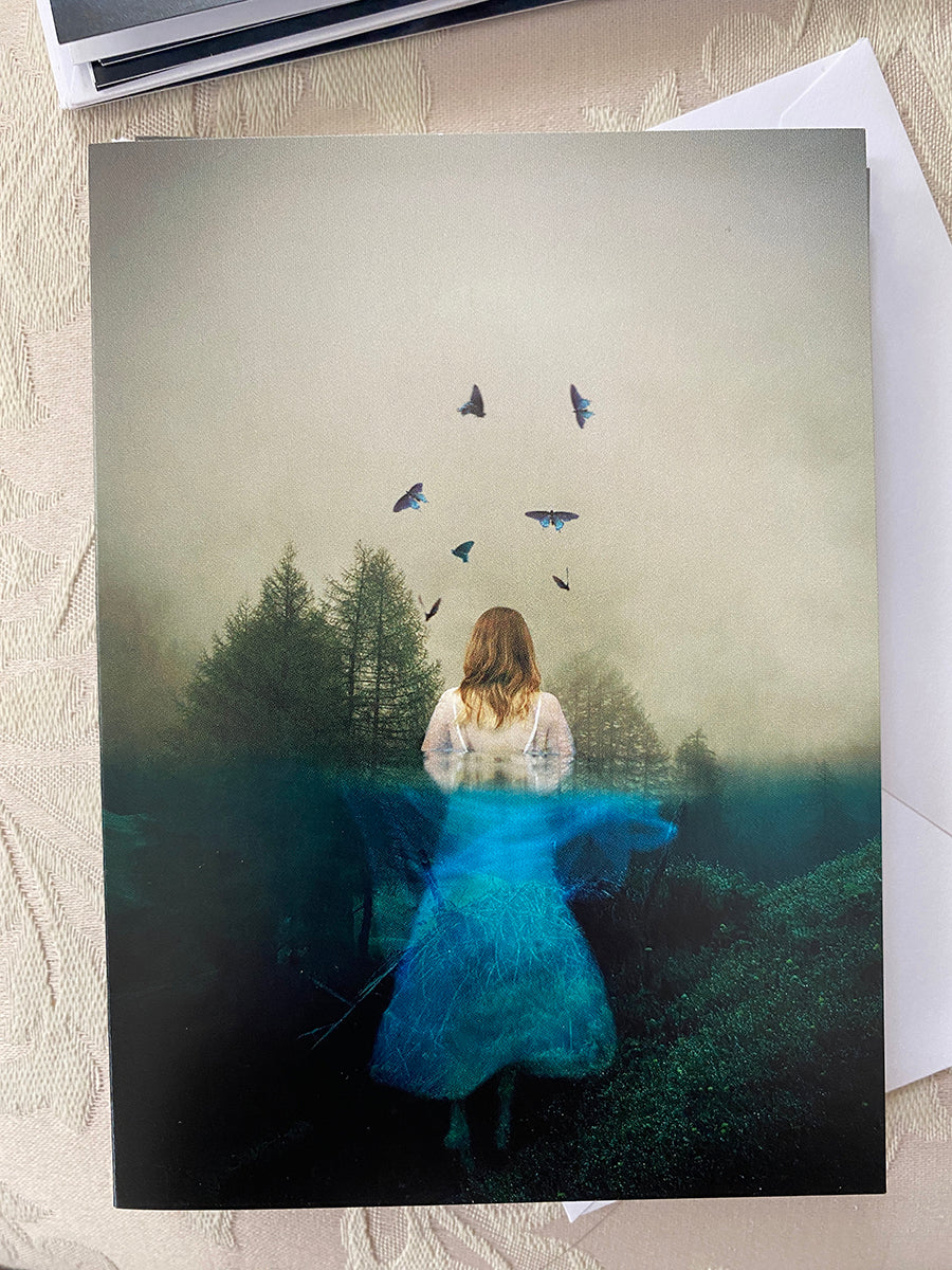 Note card featuring a fine art print with a girl in a blue dress surrounded by trees and butterflies in a mystical watery forest.