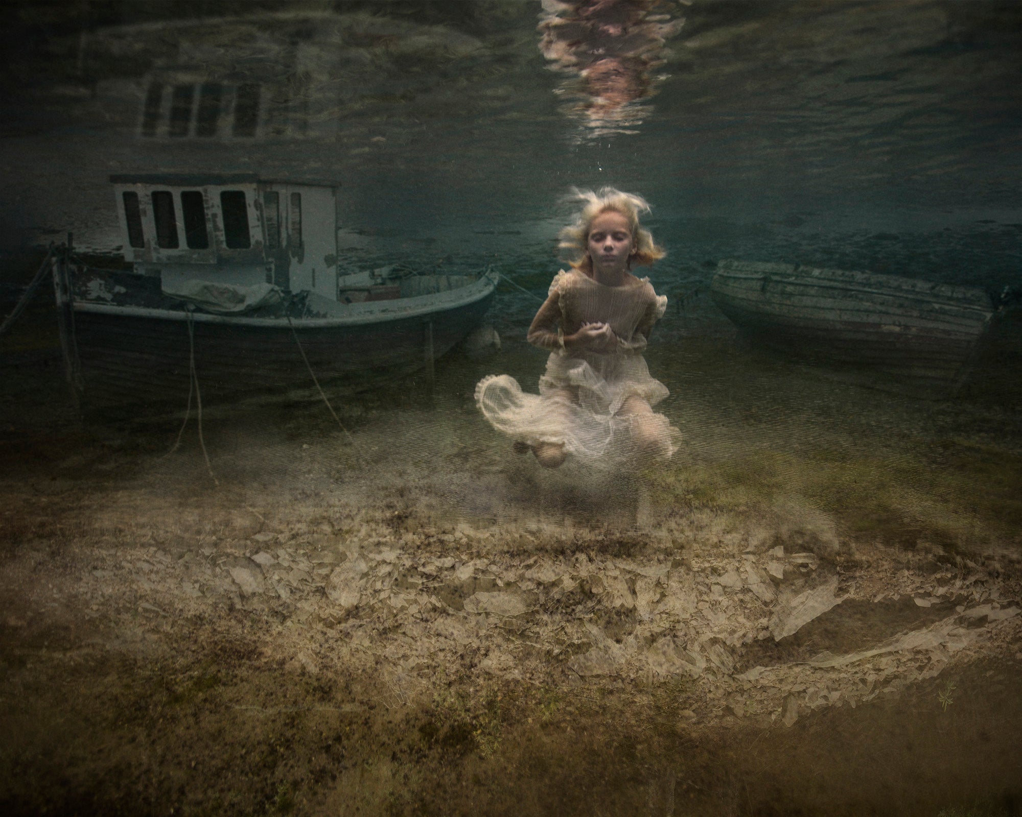 Underwater photograph featuring a young girl surrounded by boats, capturing a sense of mystery and serene exploration.