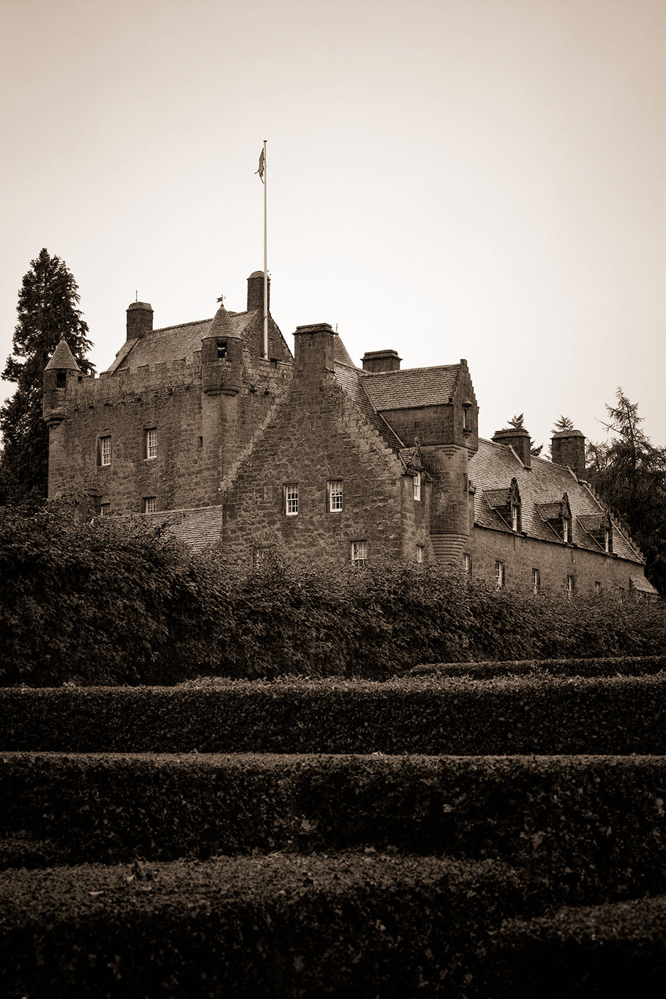 A black and white photograph of Cawdor Castle, Scotland, featuring a rugged, old stone building with a flag at the top.