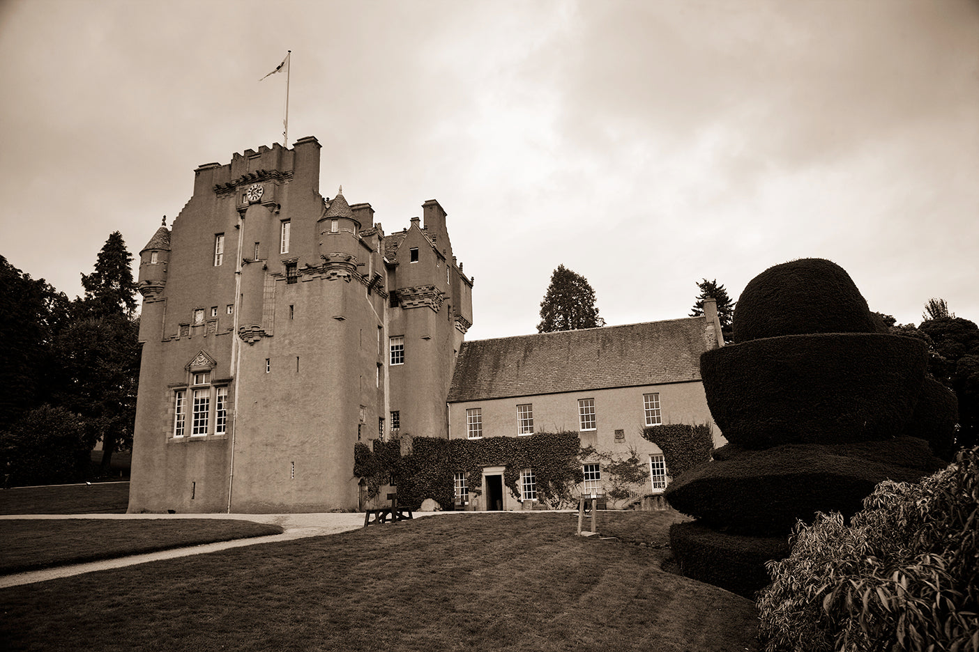 A black and white photograph of Crathes Castle, featuring a gothic architectural style with a clear sky in the background.