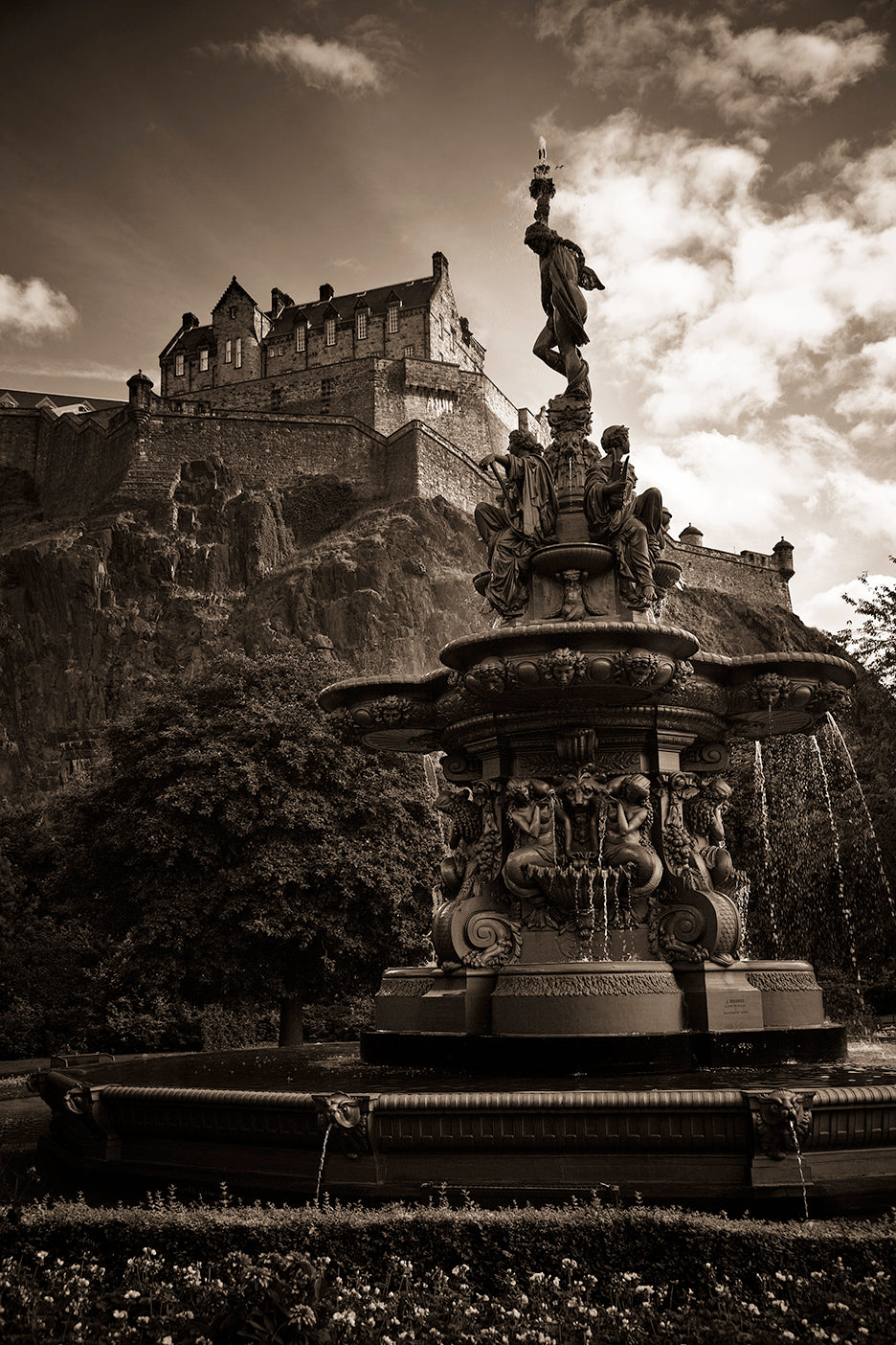 A black and white photo of Edinburgh Castle with a decorative fountain in the foreground, both are devoid of color.