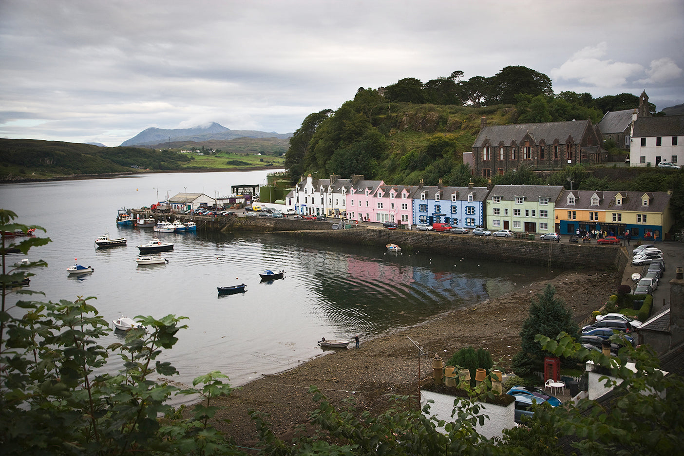 A black and white photo of Portree on Skye, showing the village with colorful buildings, boats in the harbor, and Scottish Highlands in the background.