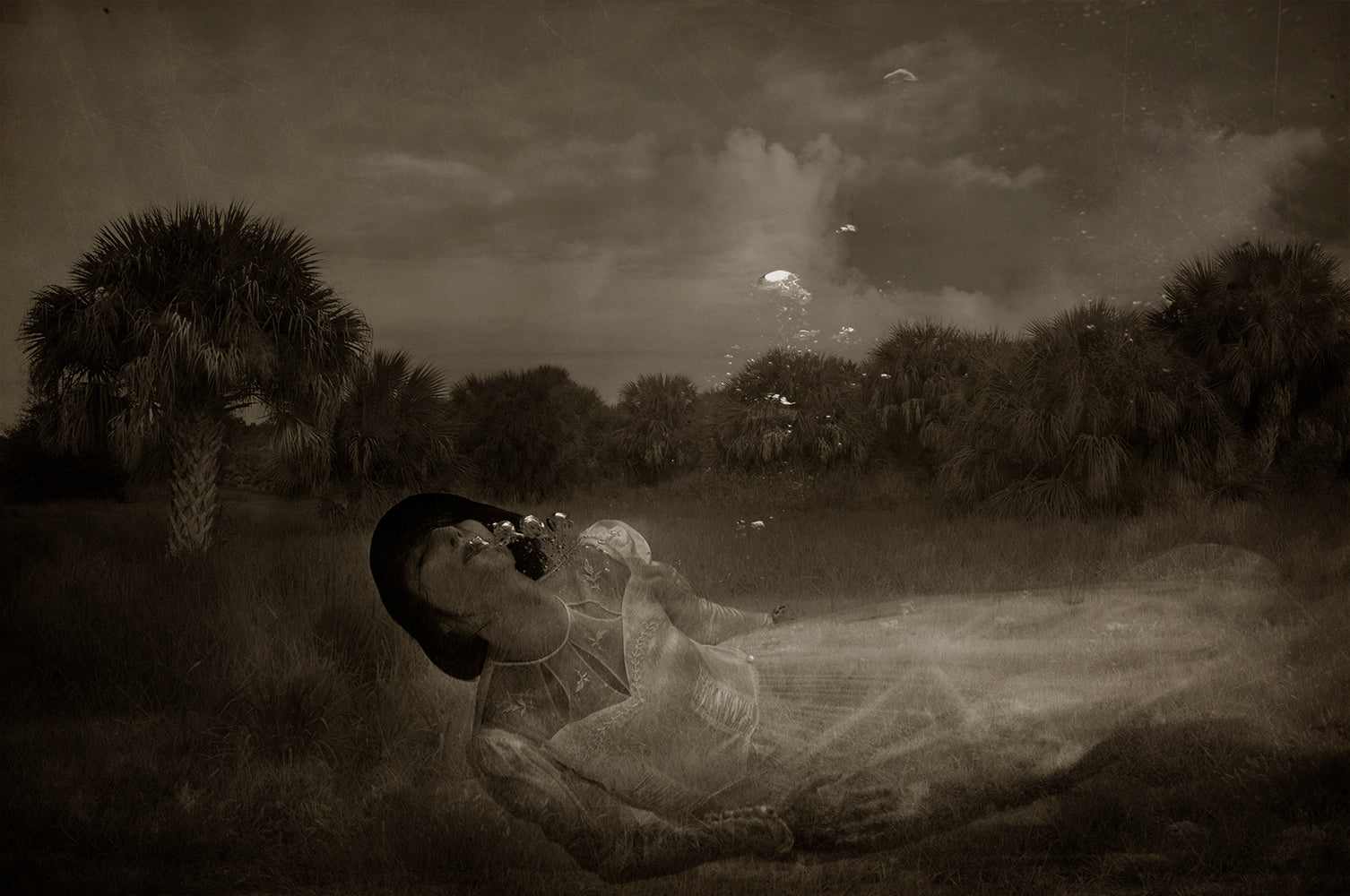 A black and white photograph featuring a person floating underwater, looking up at the sky with a dreamlike expression, overlaid with delicate, abstract patterns.