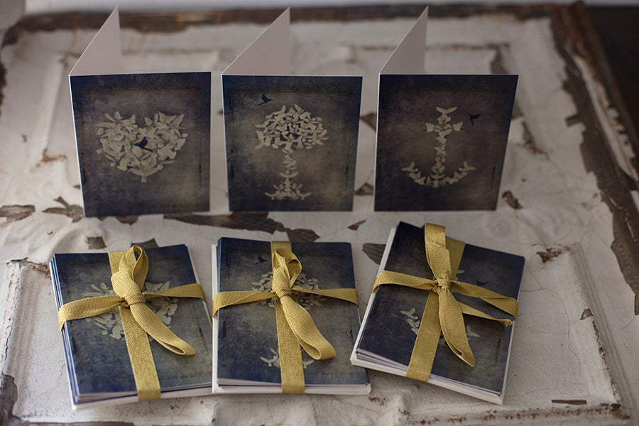 A set of six folded note cards displayed on a table, with a vintage design including doves and floral patterns, tied with gold ribbons.