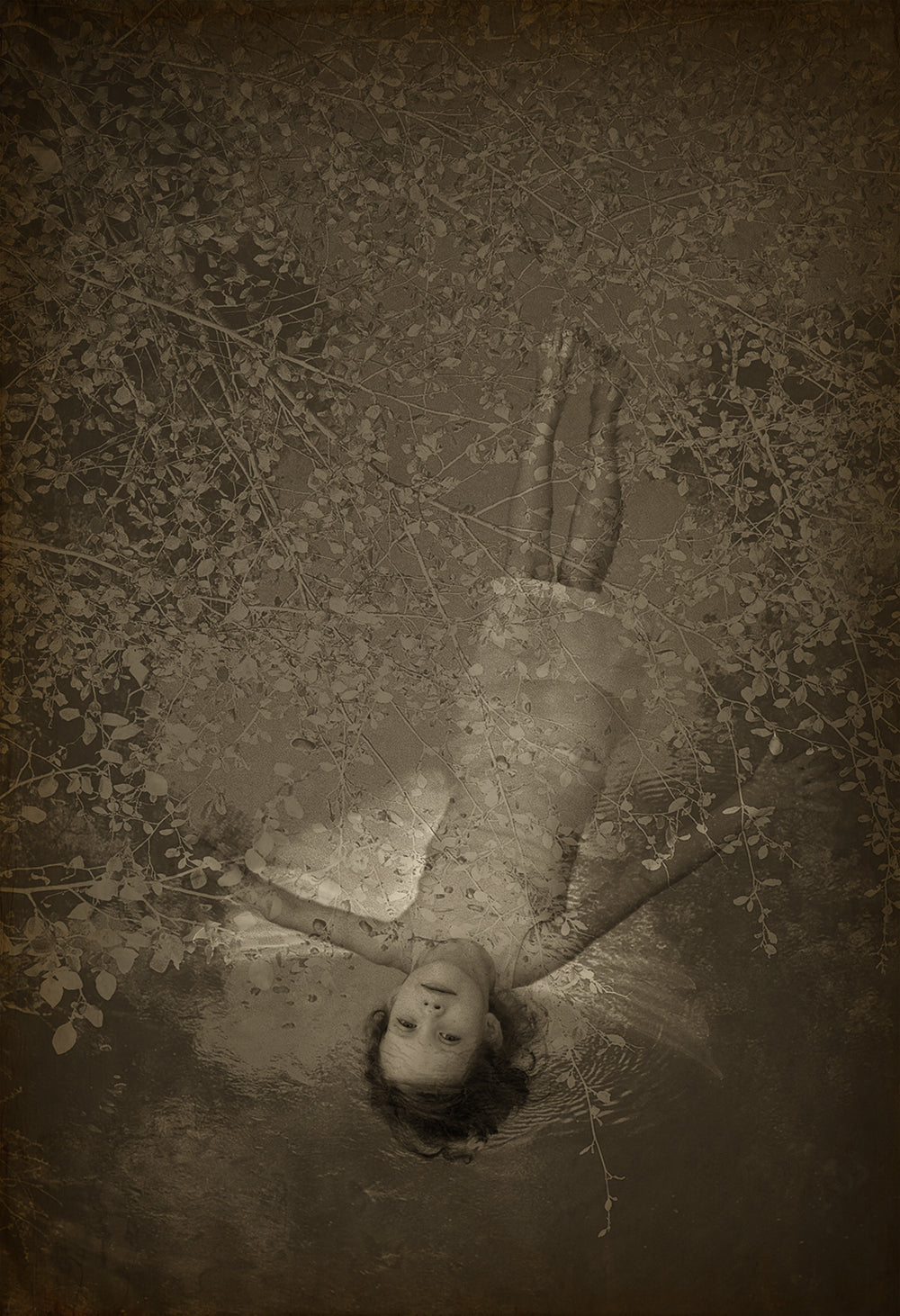 A black and white photograph of a person lying down with outstretched arms, surrounded by water droplets, creating a splash effect. The image has a vintage, sepia-toned filter.