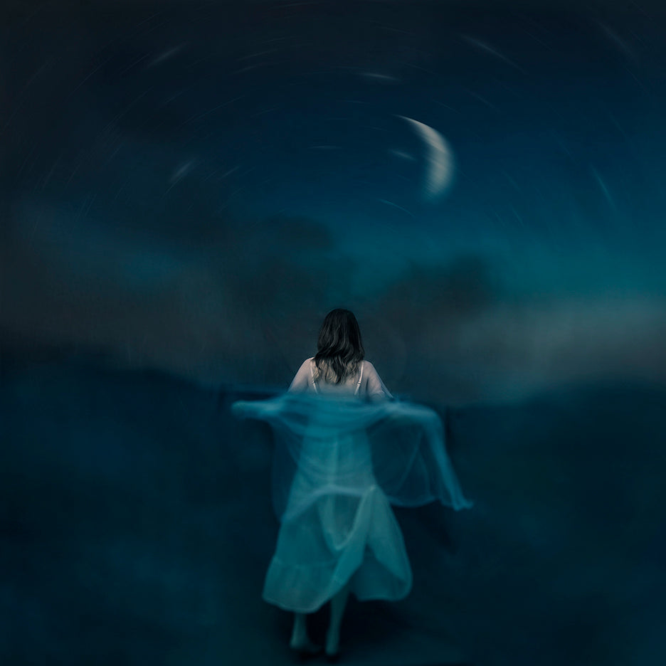 A dreamlike photograph featuring a figure in a light-colored dress standing with their back to the camera against a moonlit night sky with swirling clouds.