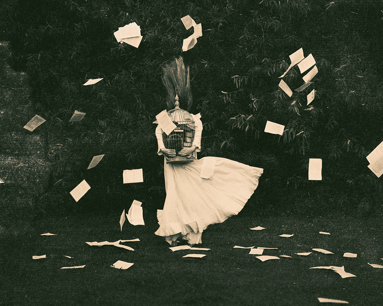 A black and white photograph of a person in a white dress, surrounded by floating papers, with a blurred background.