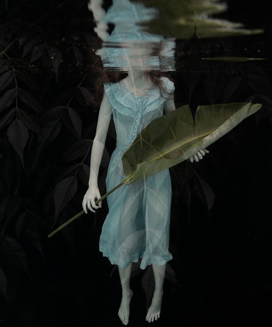 A whimsical photo of a figure underwater holding a large leaf, with a serene and mystical ambiance.