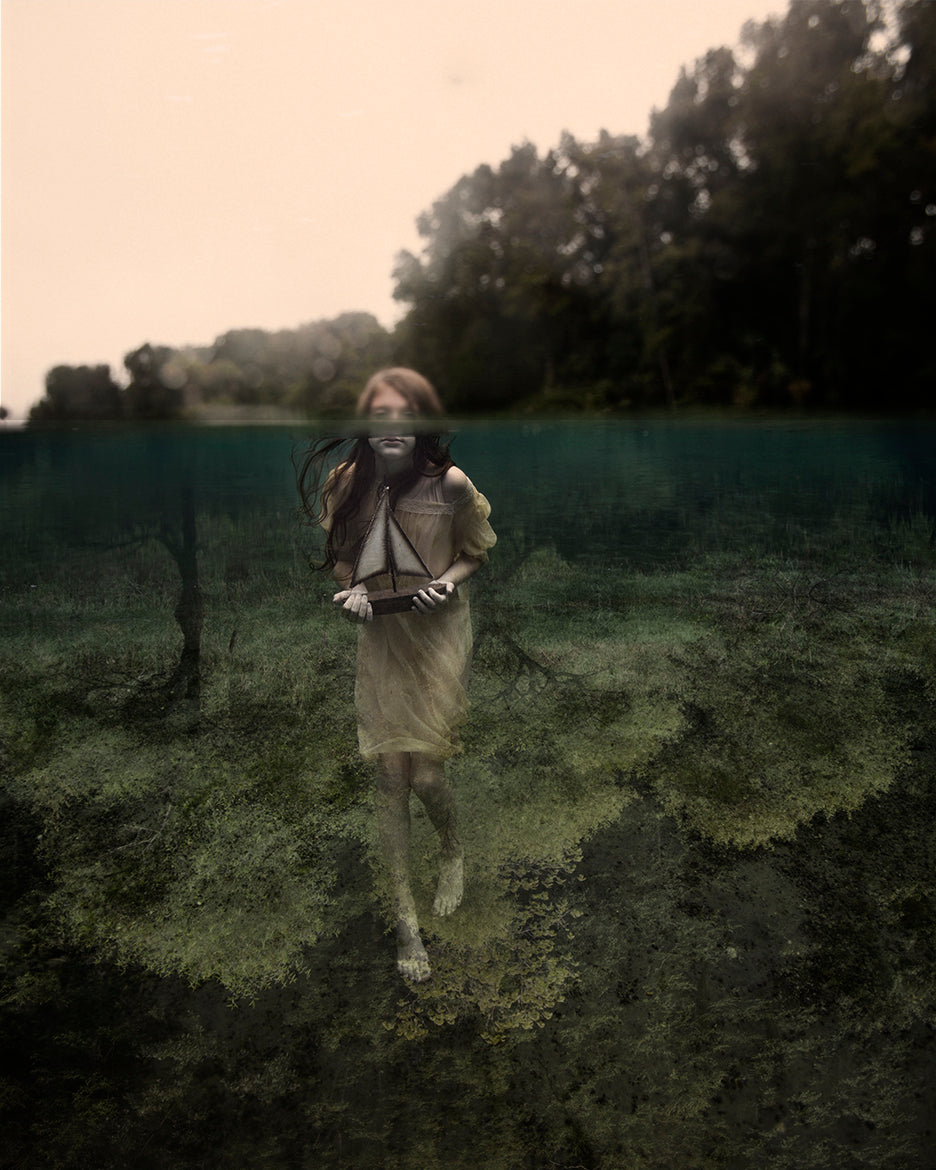 girl underwater clinging to a small model sailboat
