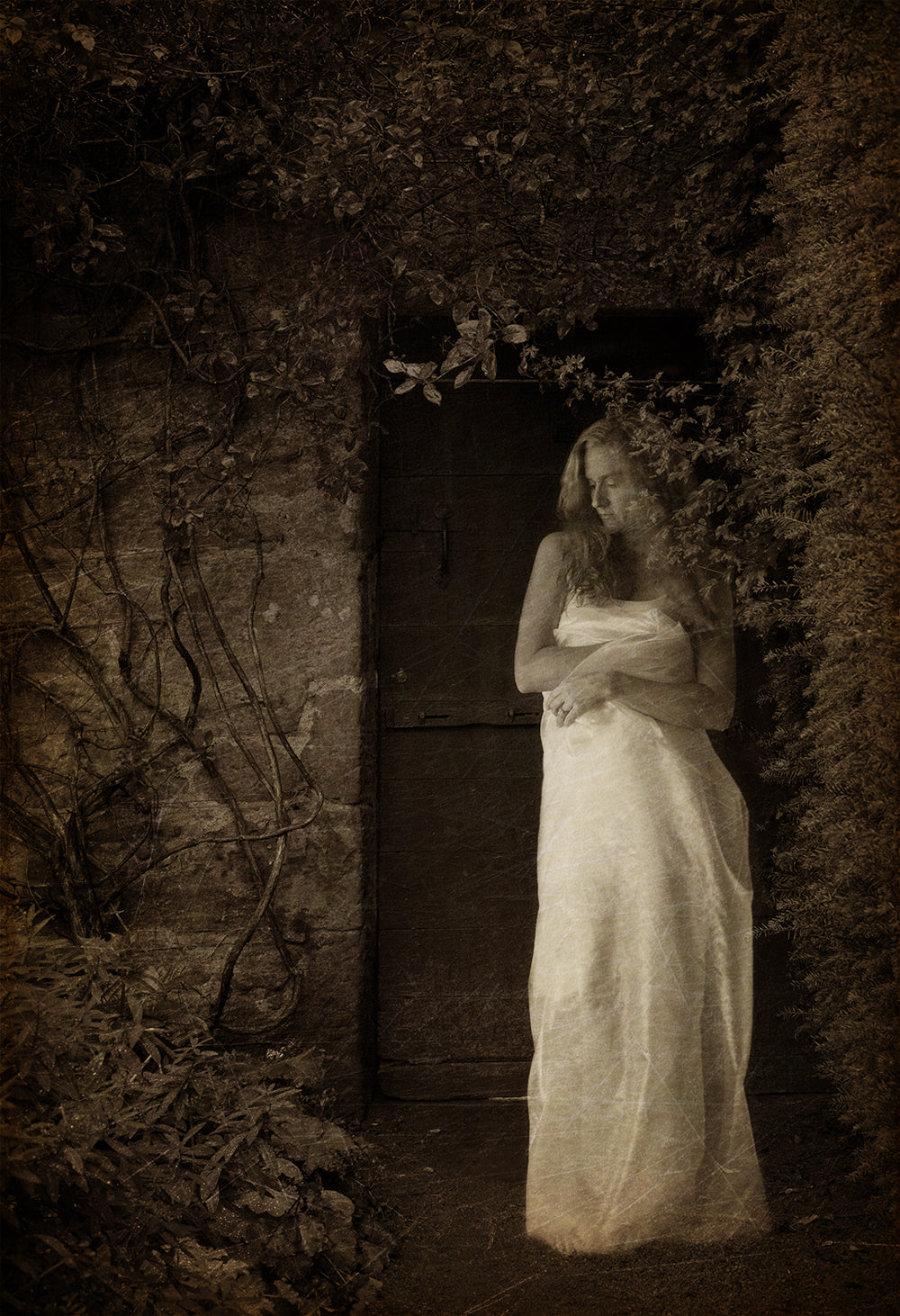 A black and white photograph of a person standing in a doorway with vines, possibly a self-portrait, with a vintage tone.