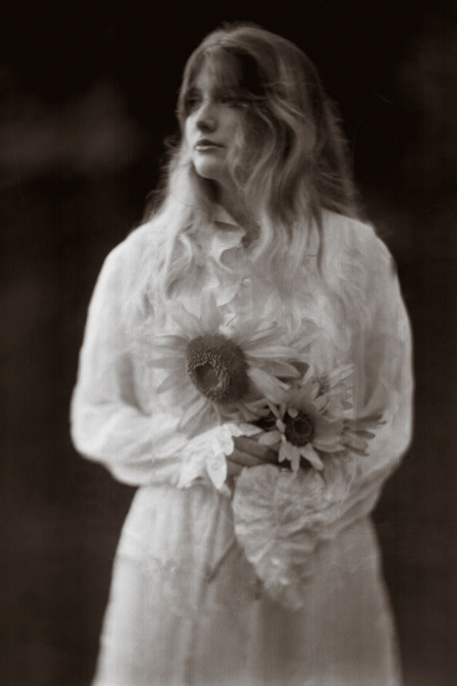A black and white photograph of a girl holding a bouquet of sunflowers, with a soft focus and sepia tone.