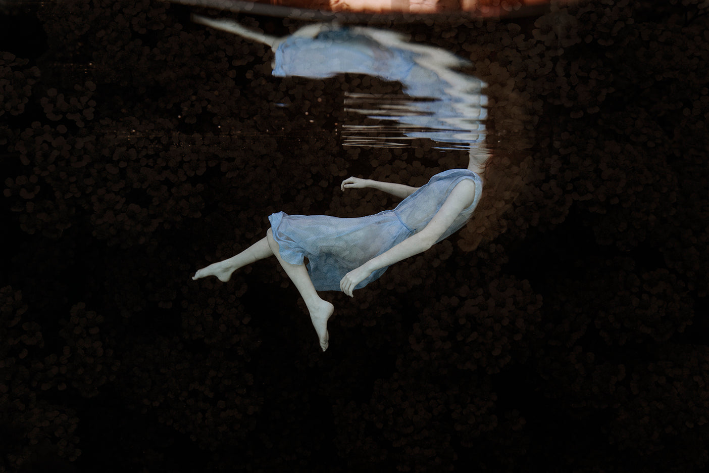 Underwater photograph featuring a figure in a pose that resembles swimming or floating, with a mystical and ethereal aesthetic.