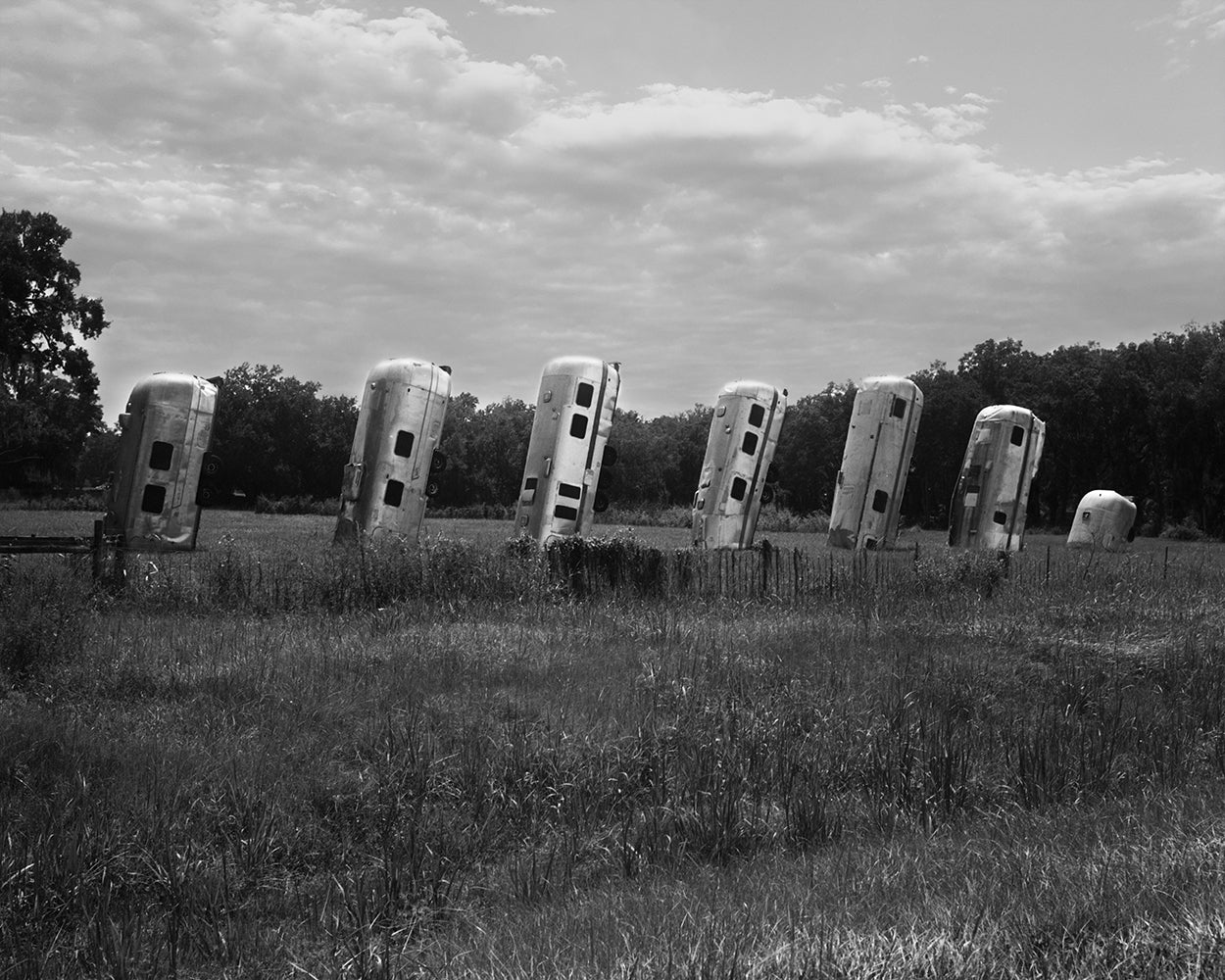 A black and white image of several vintage Airstream trailers lined up in a field.