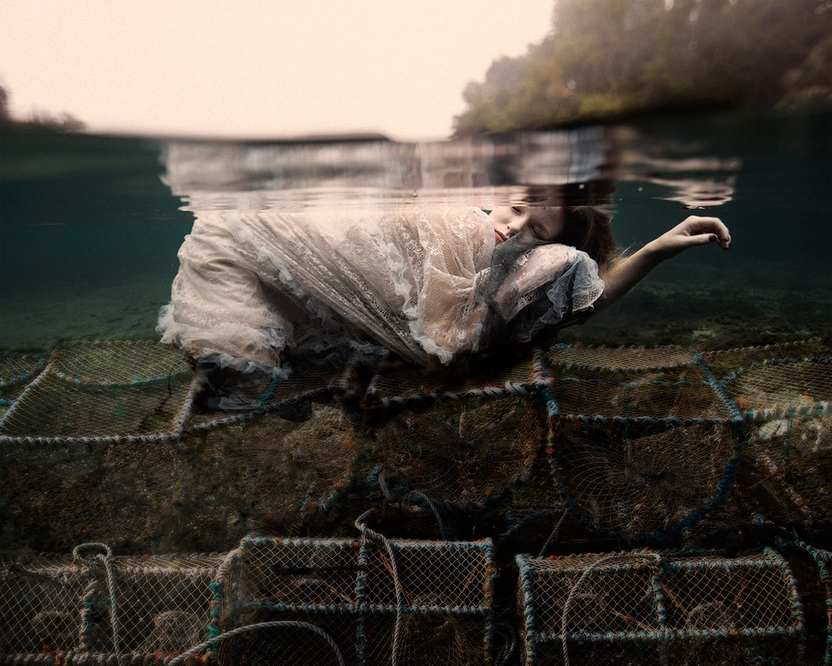 A surreal fine art photograph depicting a girl sleeping underwater atop crab traps, surrounded by a serene underwater environment with visible traps and soft lighting.