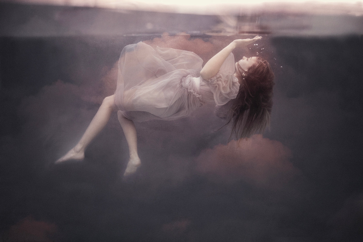 A whimsical photograph featuring a person in a dress, floating underwater with a ethereal, dreamlike quality.
