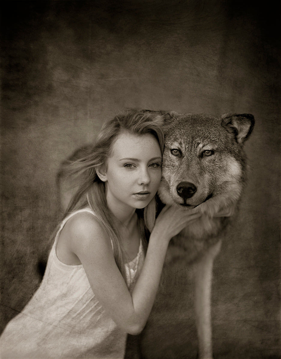 A black and white photograph featuring a woman embracing a wild wolf, with a blurred background.