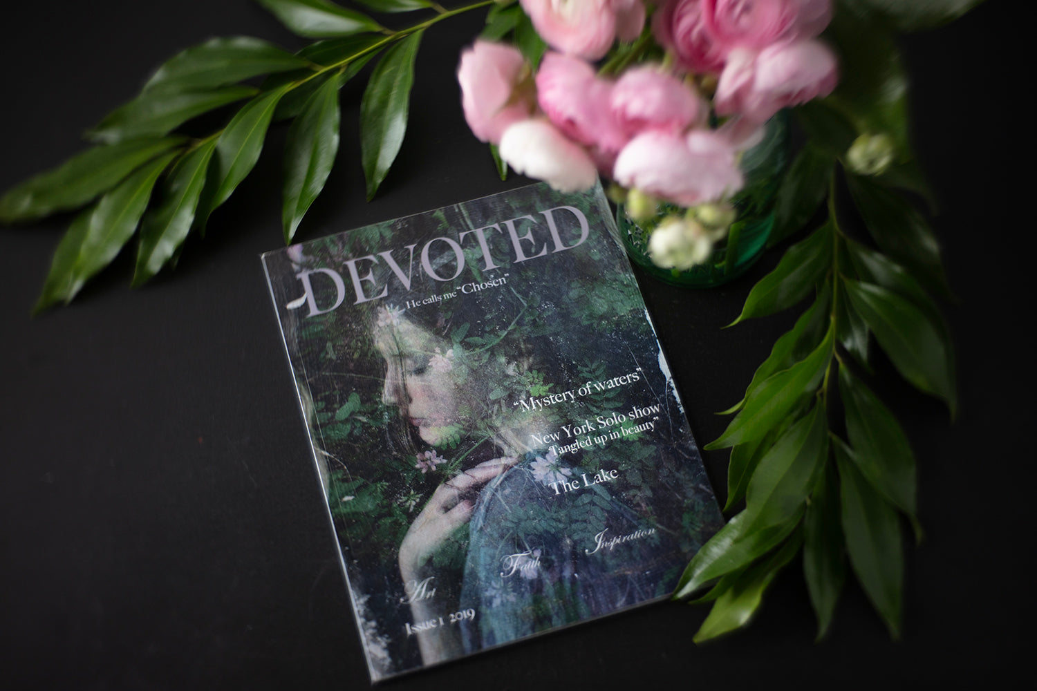 A copy of 'Devoted' magazine is displayed with a background of pink roses and green leaves, highlighting the cover photograph of a person in a vintage style.