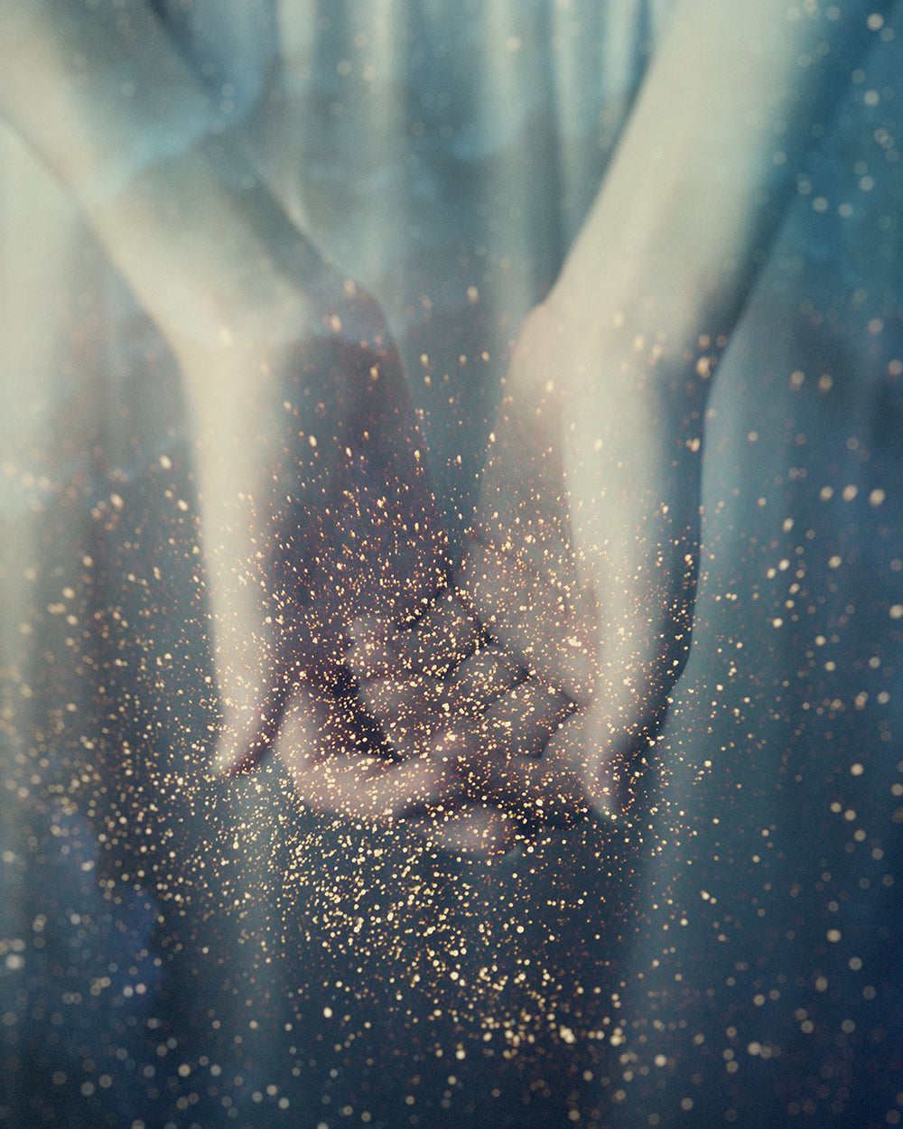 A photographic image of hands holding sparkles or dust, with a soft focus and a hazy background, representing the magical or the ethereal.