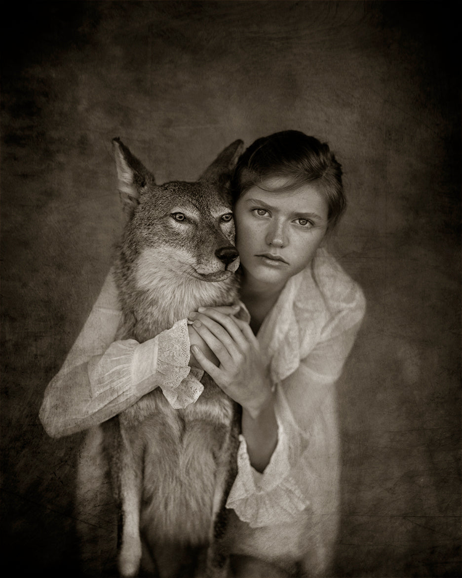 A black and white image of a person holding a coyote, in their arms.