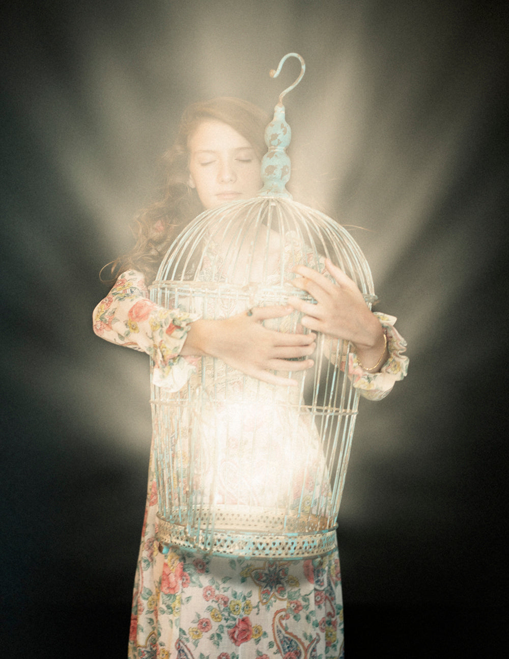 A artistic photograph of a person embracing a birdcage with a glowing light from within,Vintage style clothing and soft color palette.