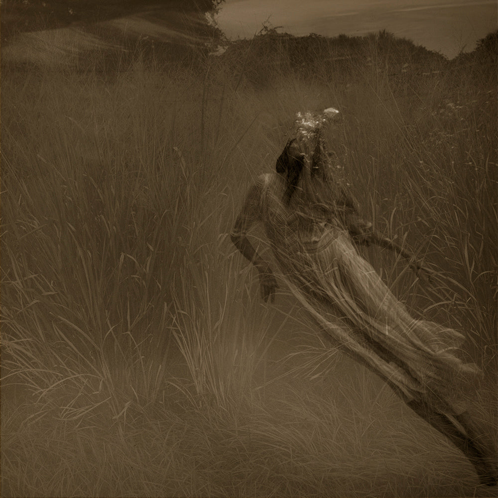 A sepia-toned photograph depicting a figure in a dress floating underwater in a grassy field with a blurred background.