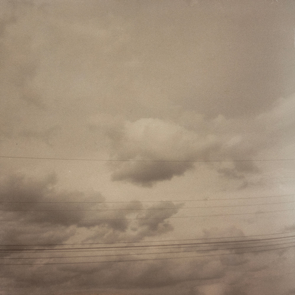 A black and white photograph of clouds in a sky, with power lines running horizontally through the image.